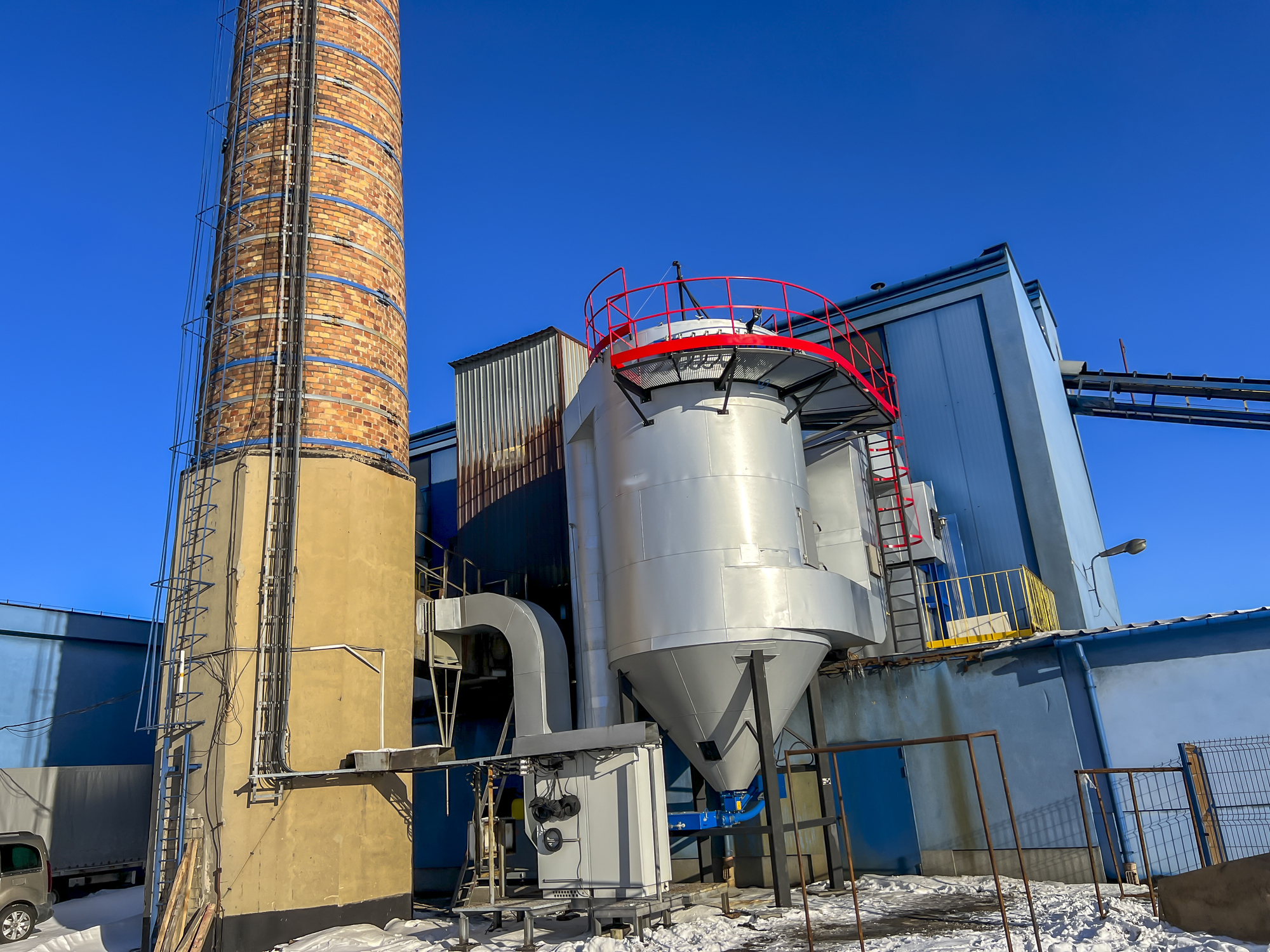 An old ceramic chimney (made of brick) and an old and new flue gas dust collector behind a coal boiler, a grate, against the blue sky.